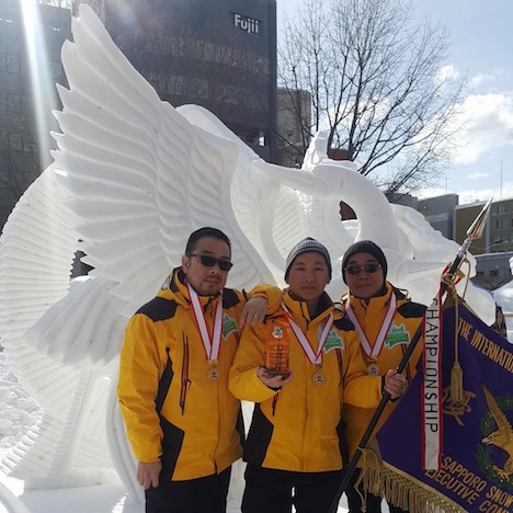 優勝旗を手に作品の前で記念撮影に臨むマカオ代表チームの3人＝2月9日、北海道札幌市（写真：MGTO）